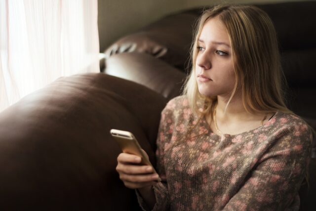 Girl,Teenager,Holding,A,Smartphone,And,Looking,Out,The,Window