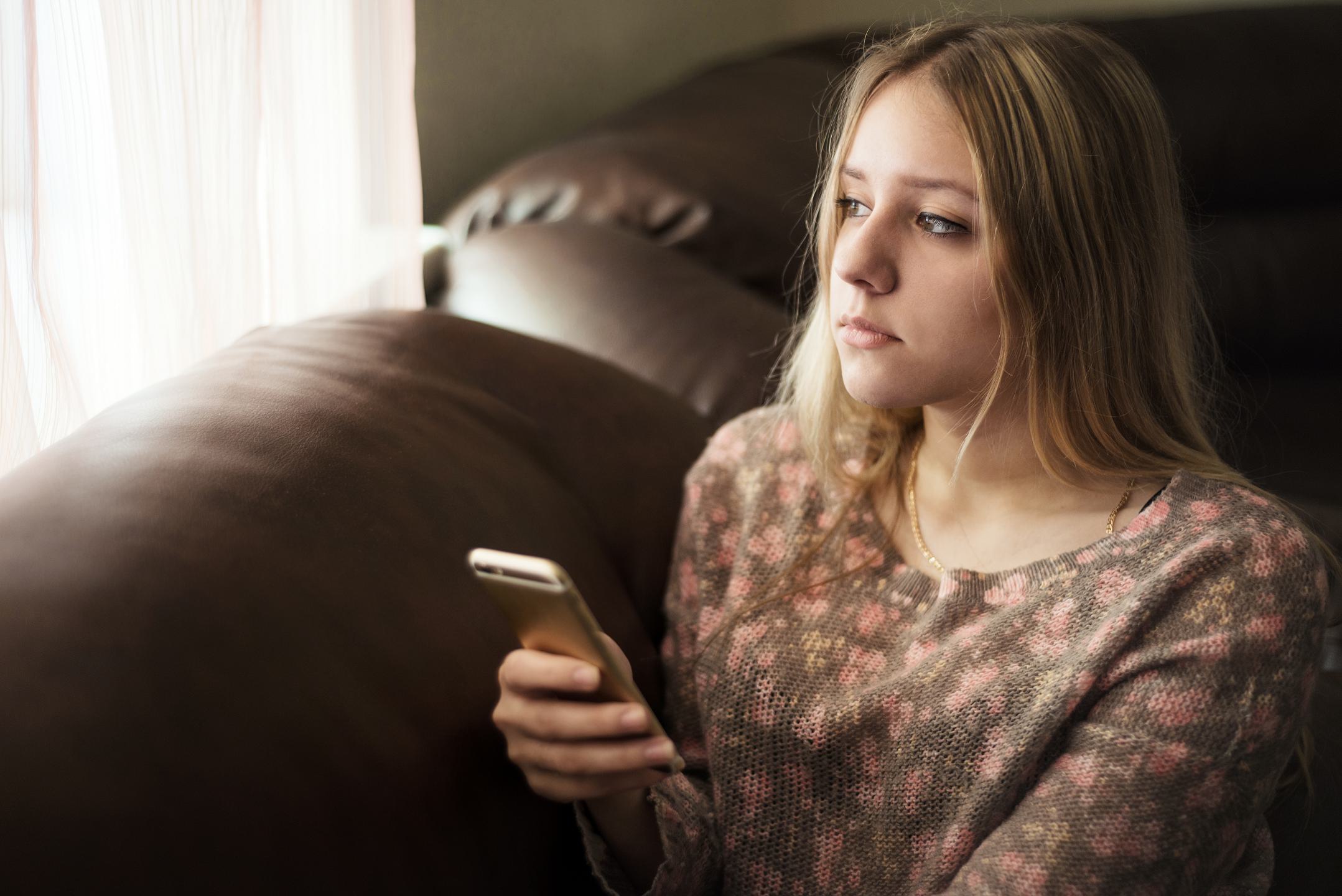 Girl,Teenager,Holding,A,Smartphone,And,Looking,Out,The,Window